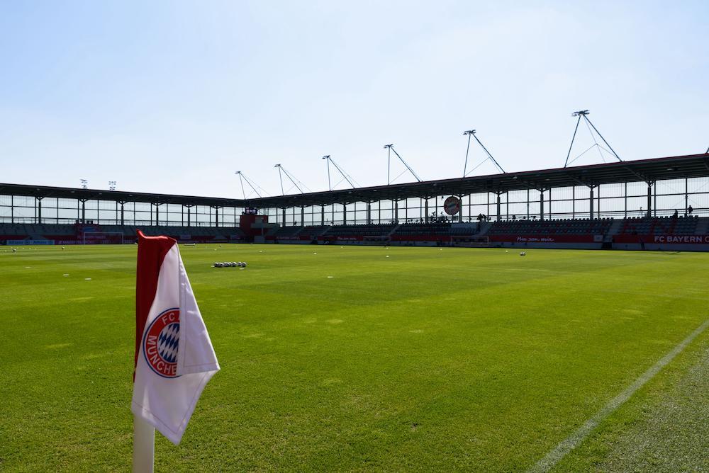 Bild des Stadions am FC Bayern Campus. Im Vordergrund ist eine Eckfahne und das Spielfeld, während im Hintergrund die Tribünen zu sehen sind.