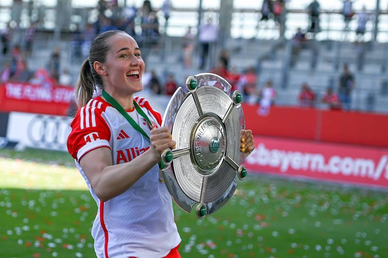 Eine Spielerin des FC Bayern feiert mit der Meisterschale vor der Fankurve.